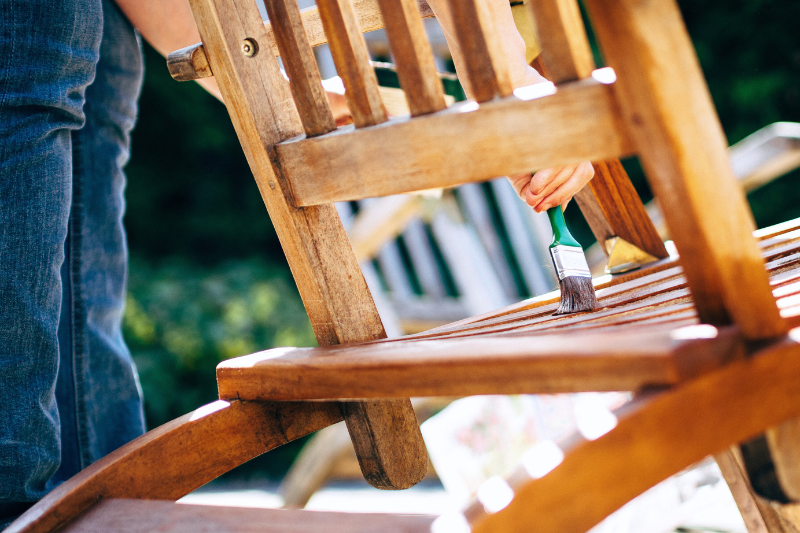 A person painting a wooden chair with a brush, focused on the seat.