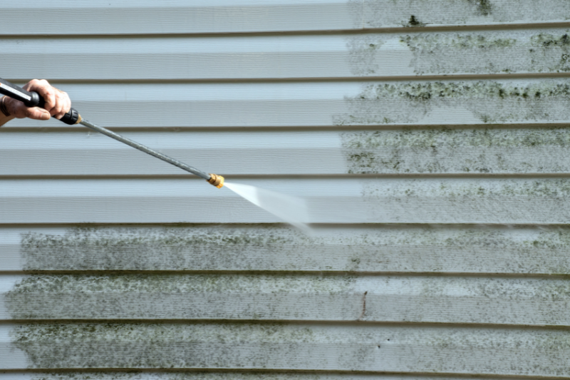 Person using power washer to spray mold from house siding.