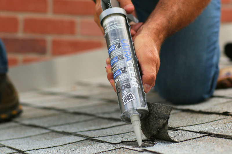Person applying DAP ULTRA CLEAR sealant to reattach lifted shingle.