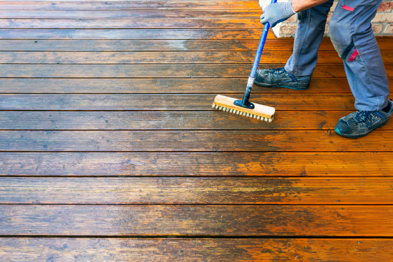 Scrubbing dirty deck with long-handled stiff wire brush.
