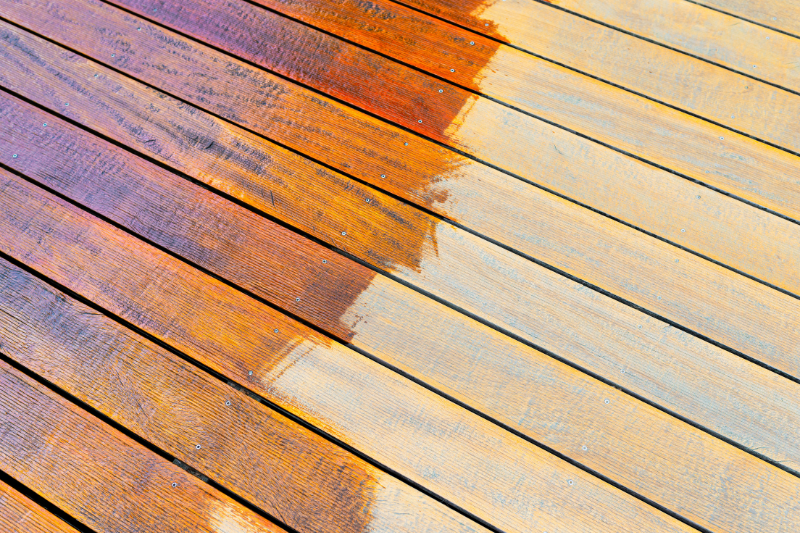 Close up of deck boards, half stained a reddish brown colour.