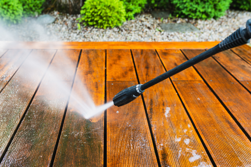 Close up of deck being power washed, surface is wet and half cleaned.