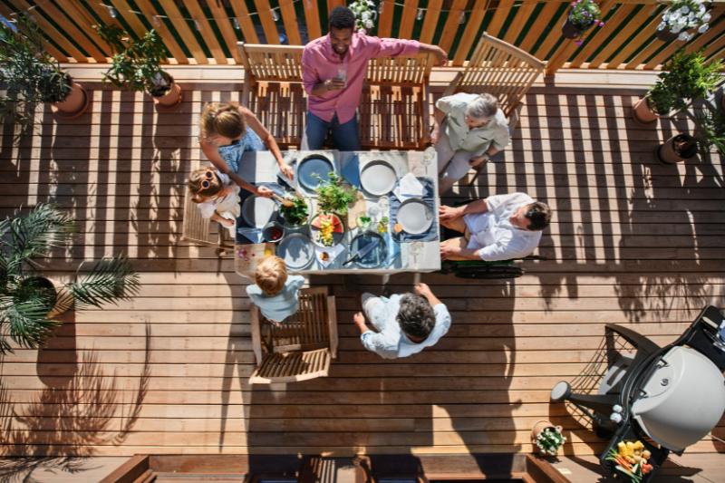 Birds eye view of family enjoying dinner on a sunny wooden terrace.