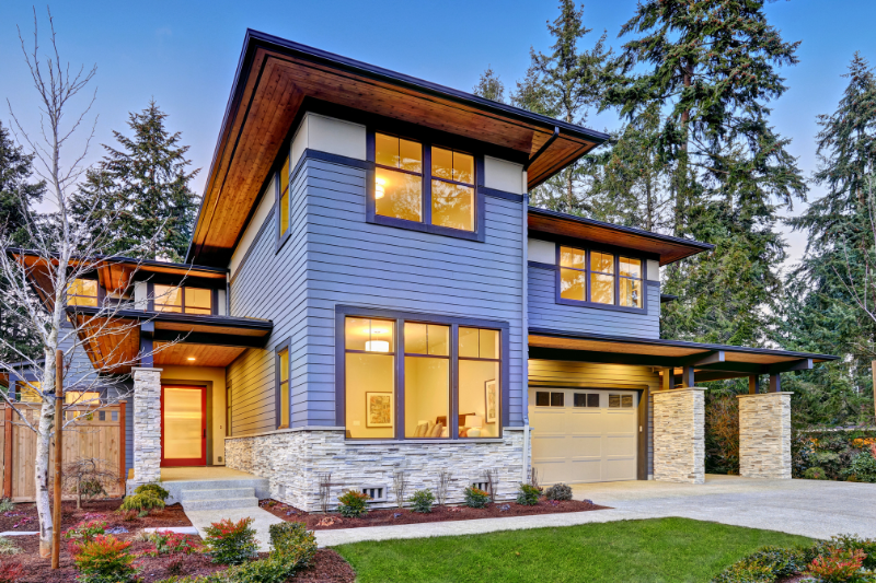 A modern blue house with large, black framed windows, stone accents, and a green lawn.