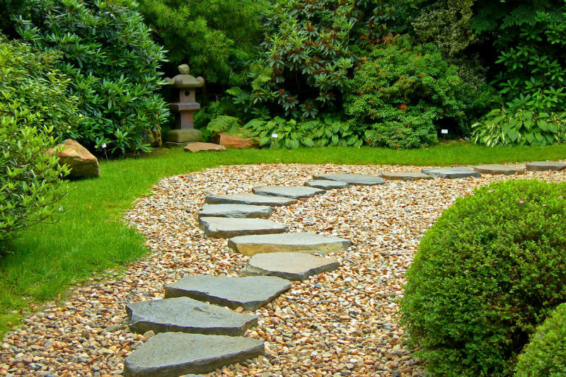 A curving flagstone path is nestled in gravel, surrounded by a lush green lawn with greenery all around.